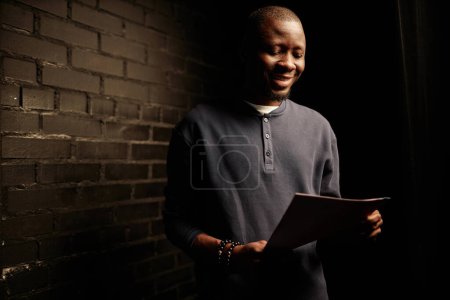 Téléchargez les photos : Portrait taille haute d'un homme afro-américain souriant répétant des lignes tout en se préparant pour le spectacle dans les coulisses de l'espace de copie - en image libre de droit