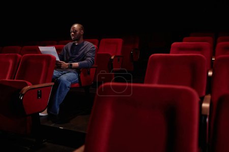 Foto de Retrato mínimo del artista afroamericano sentado en la audiencia y leyendo líneas en el espacio de copia del teatro vacío - Imagen libre de derechos
