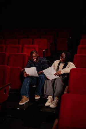 Foto de Retrato vertical de dos artistas afroamericanos sonrientes sentados en el suelo en el teatro y ensayando para el espacio de copia del espectáculo - Imagen libre de derechos