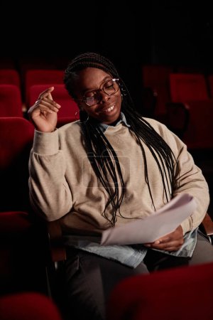 Téléchargez les photos : Portrait vertical d'un artiste afro-américain souriant lisant le script se préparant pour une représentation au théâtre - en image libre de droit