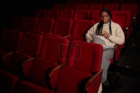 Foto de Retrato mínimo de la mujer negra adulta leyendo guion en público en el teatro en espacio de copia de poca luz - Imagen libre de derechos