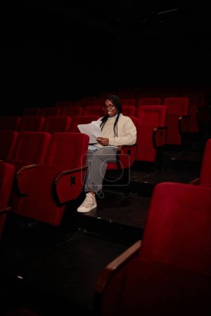 Foto de Retrato vertical de larga duración de una mujer joven sola en audiencia preparándose para el espectáculo y el guion de lectura - Imagen libre de derechos