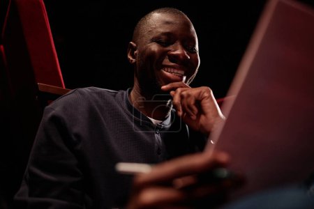 Foto de Retrato de bajo ángulo del artista afroamericano sonriente leyendo líneas y sonriendo preparándose para el espectáculo - Imagen libre de derechos