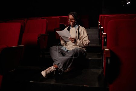 Foto de Retrato de larga duración de la artista negra leyendo líneas sentadas en el suelo en el espacio de copia del teatro - Imagen libre de derechos