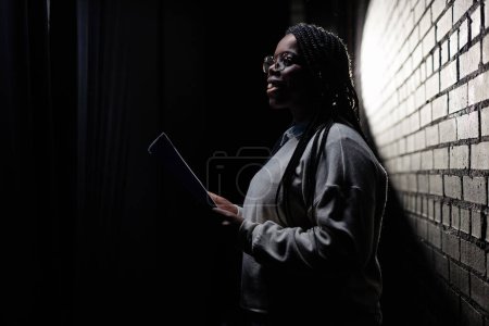 Foto de Retrato de vista lateral mínima de una joven negra ensayando en el escenario en teatro con espacio de copia de poca luz - Imagen libre de derechos