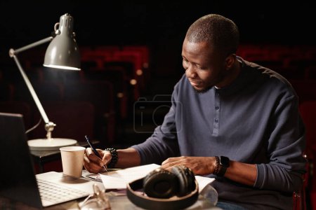 Portrait of African American man as director in theater taking notes and reading script copy space