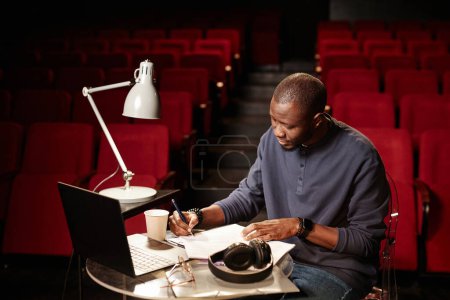 High angle portrait of theater director reading script at table in audience copy space
