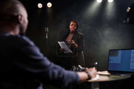 Porträt einer schwarzen jungen Frau, die auf der Bühne mit einem Theaterregisseur auftritt, der Proben oder Castings beobachtet