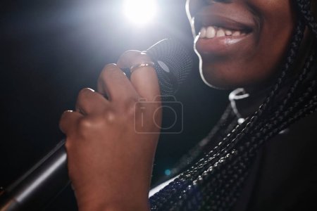 Photo for Close up of smiling Black woman holding microphone on stage with spotlight copy space - Royalty Free Image
