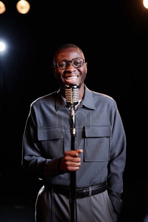 Vertical portrait of smiling African American man speaking to microphone on stage performing in comedy show