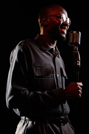 Vertical side view portrait of smiling Black man speaking to microphone on stage performing in stand up show