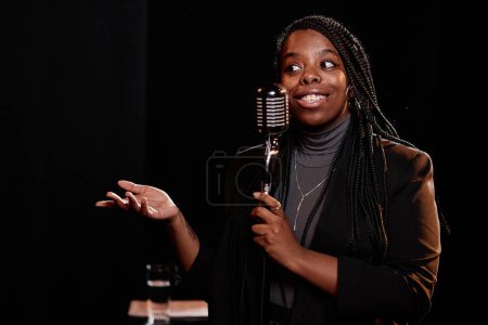 Téléchargez les photos : Portrait taille haute de jeune femme noire parlant au microphone performant dans stand up montrer l'espace de copie - en image libre de droit