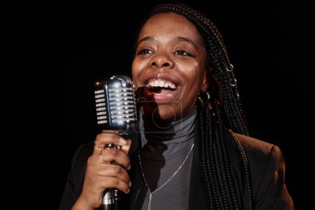 Front view portrait of Black woman singing to microphone performing on stage in theater