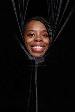 Téléchargez les photos : Portrait vertical de souriante femme noire regardant des rideaux sur la scène de théâtre - en image libre de droit