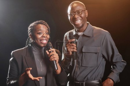 Cintura para arriba de pareja afroamericana en el escenario hablando con el micrófono junto con el foco