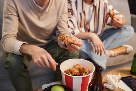 Photo for Closeup young couple eating fried chicken takeout while watching TV at home, copy space - Royalty Free Image