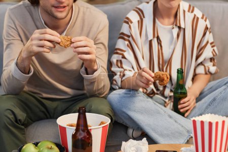 Téléchargez les photos : Gros plan jeune couple méconnaissable manger du poulet frit fast food tout en regardant la télévision à la maison - en image libre de droit