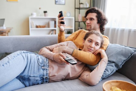 Foto de Retrato de pareja joven abrazándose en el sofá en casa y viendo la televisión juntos, espacio para copiar - Imagen libre de derechos