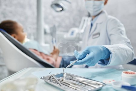 Téléchargez les photos : Gros plan d'une dentiste tenant des outils métalliques stériles pendant qu'elle travaille avec un enfant en clinique dentaire, espace de copie - en image libre de droit
