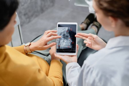 Photo for Top view closeup of dentist holding tablet with X ray images while consulting patient on dental surgery, copy space - Royalty Free Image