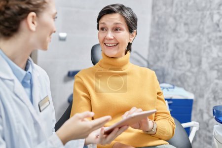Foto de Retrato de una mujer madura sonriente en una clínica dental hablando con una dentista y sosteniendo la tableta - Imagen libre de derechos