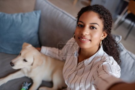 Téléchargez les photos : Portrait grand angle de jeune femme noire prenant des photos selfie avec chiot labrador à la maison, espace de copie - en image libre de droit