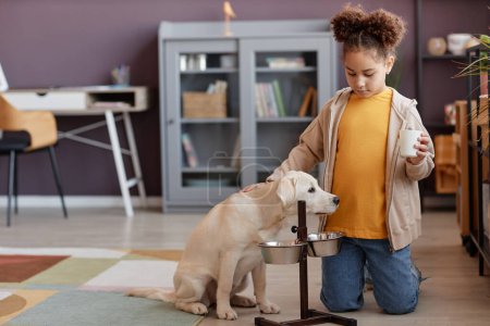 Photo for Full length portrait of cute black girl feeding puppy at home and caring for pet, copy space - Royalty Free Image