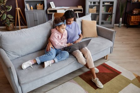 Foto de Retrato de alto ángulo de la madre y la hija usando el ordenador portátil juntos sentados en el sofá en el hogar acogedor, espacio de copia - Imagen libre de derechos