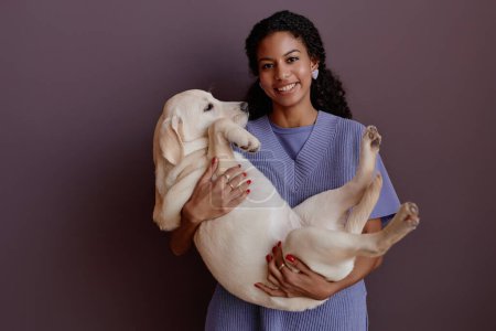 Téléchargez les photos : Portrait à la taille minime d'une jeune femme noire tenant un chien et souriant à la caméra - en image libre de droit