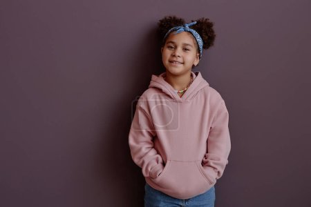 Téléchargez les photos : Taille minime portrait de mignonne fille noire souriant à la caméra portant un sweat à capuche rose, espace de copie - en image libre de droit