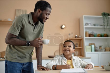 Foto de Feliz retrato diario de padre e hijo negros en la cocina juntos dibujando o haciendo tarea - Imagen libre de derechos