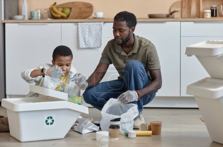Foto de Retrato completo del padre y el hijo afroamericanos clasificando papel y plástico para reciclar en casa - Imagen libre de derechos