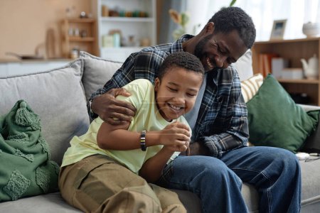 Photo for Candid portrait of playful father and son sitting on couch together and enjoying family time - Royalty Free Image