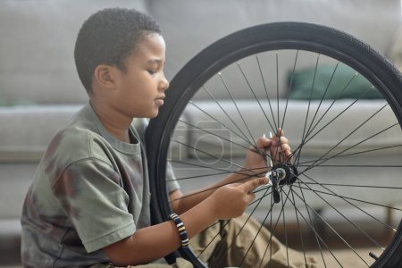 Photo for Side view portrait of African American young boy repairing bicycle wheel and checking tires, copy space - Royalty Free Image