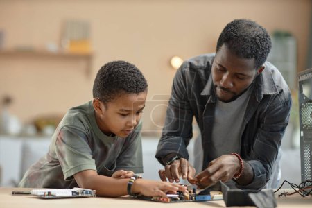 Photo for Portrait of African American father and son repairing computer parts together at home, copy space - Royalty Free Image