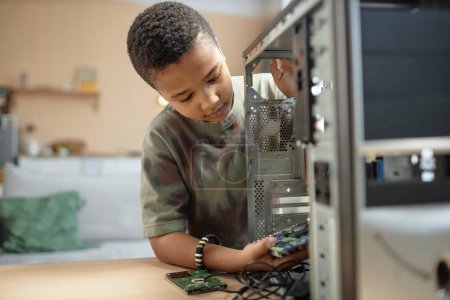 Téléchargez les photos : Portrait d'un jeune garçon afro-américain construisant un ordinateur PC et assemblant des pièces, espace de copie - en image libre de droit