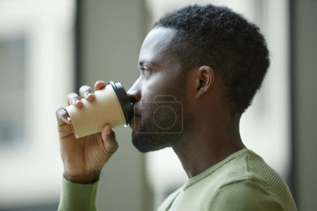 Foto de Vista lateral primer plano del hombre negro beber café con taza de papel contra el fondo borroso mínimo - Imagen libre de derechos