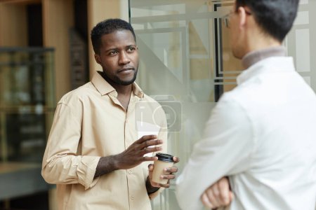 Photo for Waist up portrait of confident Black young man chatting with colleague during coffee break in modern office - Royalty Free Image