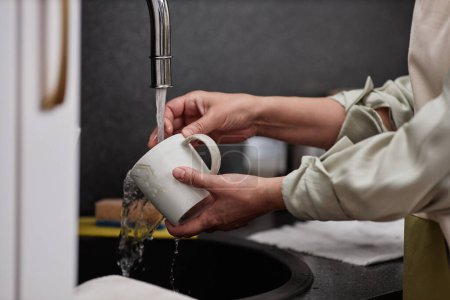 Foto de Primer plano de mujer irreconocible lavando taza de café en agua del grifo en la cocina, espacio de copia - Imagen libre de derechos