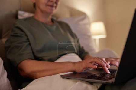 Primeros planos de la mujer mayor utilizando el ordenador portátil mientras está acostado en la cama en casa, espacio de copia