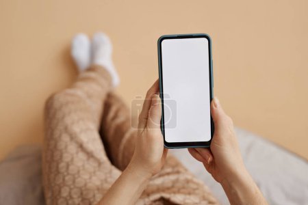 Foto de Primer plano mínimo de las manos femeninas sosteniendo el teléfono inteligente con la maqueta de pantalla blanca disfrutando de un tiempo relajante en casa, espacio para copiar - Imagen libre de derechos