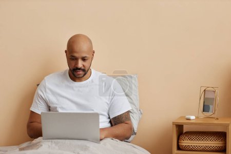 Photo for Minimal portrait of adult black man using laptop in bed in morning, copy space - Royalty Free Image