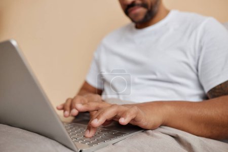 Close up of black man using laptop in bed at home with focus on male hands typing, copy space