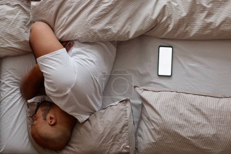 Minimal top view of black man sleeping in bed with white screen smartphone mockup, copy space