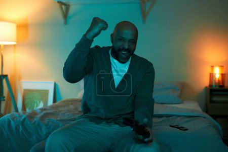Téléchargez les photos : Portrait avant de l'homme noir adulte excité jouant à des jeux vidéo dans l'obscurité et célébrant la victoire, espace de copie - en image libre de droit