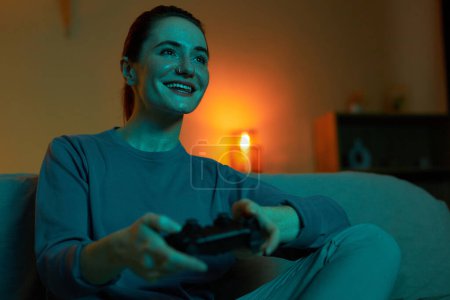 Téléchargez les photos : Portrait de femme adulte souriante jouant à des jeux vidéo dans l'obscurité et tenant contrôleur, espace de copie - en image libre de droit