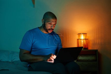 Foto de Retrato del hombre negro adulto usando el ordenador portátil en la cama por la noche hasta tarde - Imagen libre de derechos