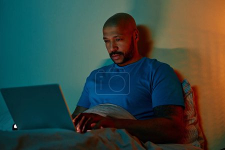 Foto de Retrato del hombre negro adulto usando el ordenador portátil en la cama por la noche que sufre de insomnio - Imagen libre de derechos