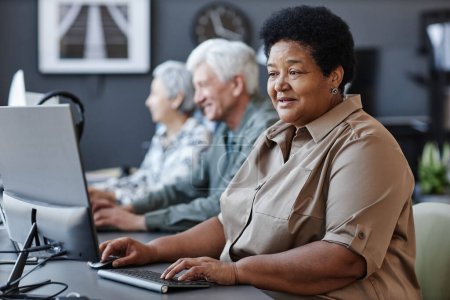 Téléchargez les photos : Portrait latéral de personnes âgées utilisant des ordinateurs en rangée avec une femme âgée noire tapant au premier plan, espace de copie - en image libre de droit