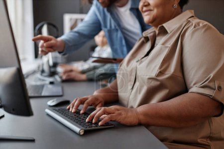 Téléchargez les photos : Gros plan de femme âgée noire utilisant un ordinateur avec professeur en classe d'informatique, espace de copie - en image libre de droit